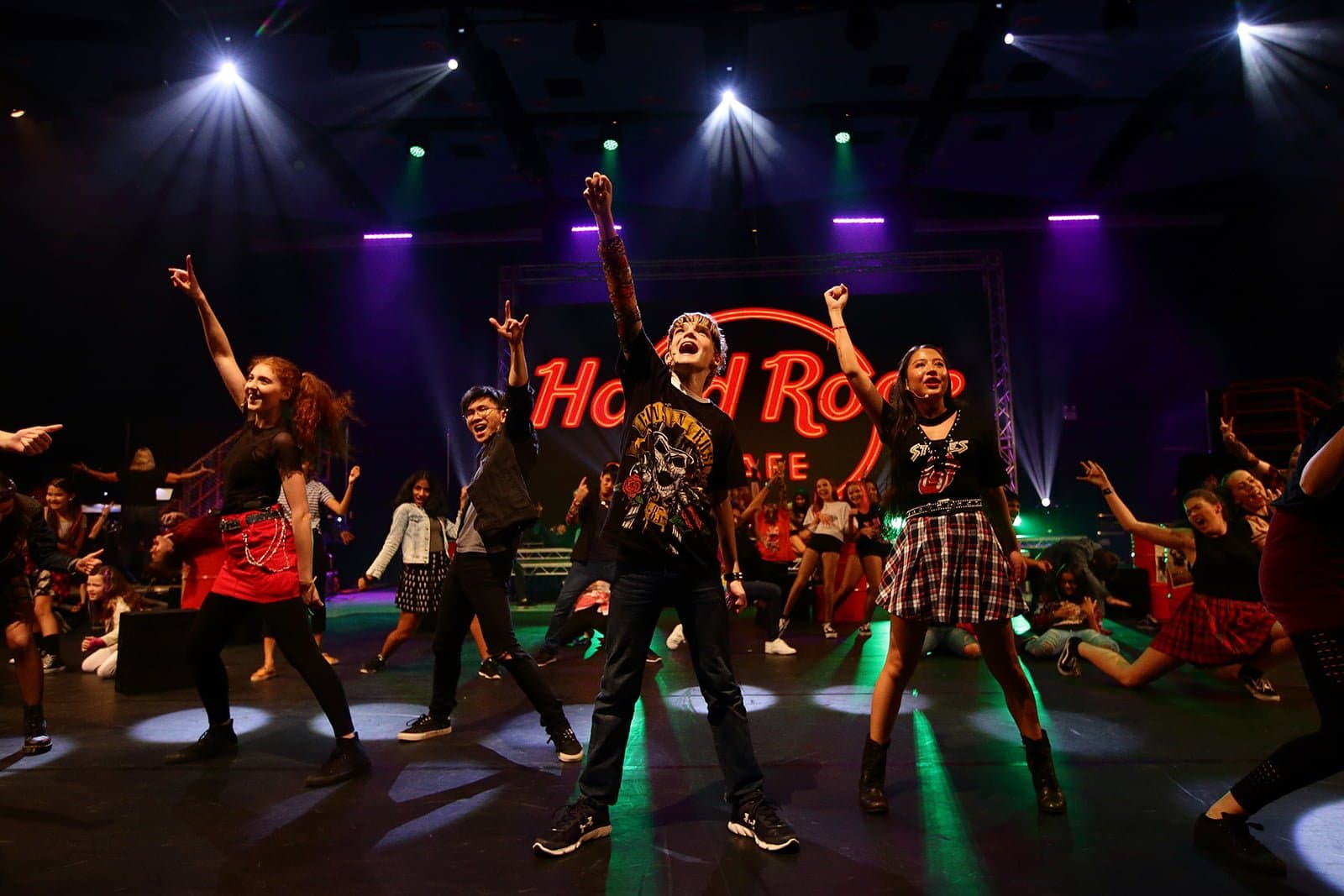 Ensemble performing on a lit stage with Hard Rock signage behind them.